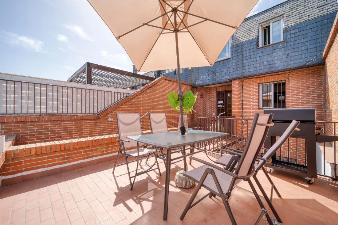 Terraza con suelo de barro, mesa con sombrilla y muro de ladrillo