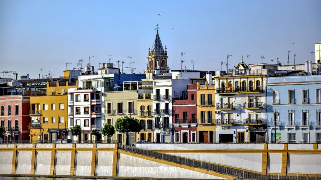 Fachadas de colores de la calle Betis sobre el río, con un campanario al fondo