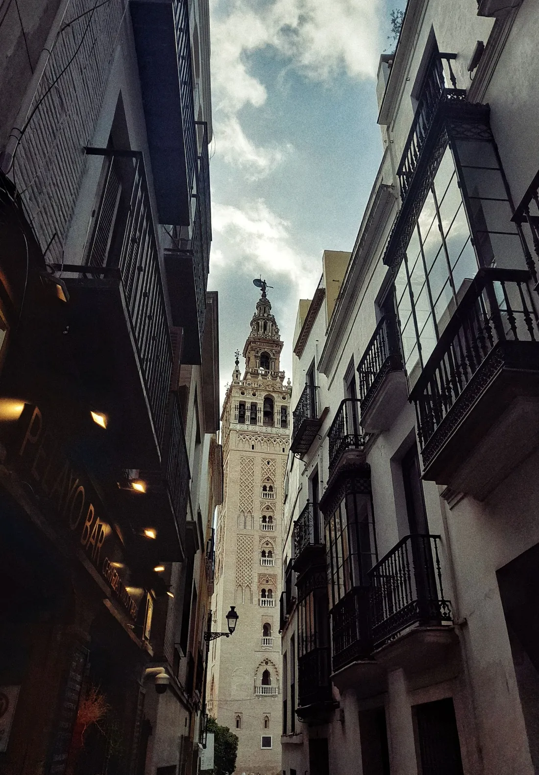 Calle estrecha del centro con cierros y balcones de forja y la Giralda al fondo