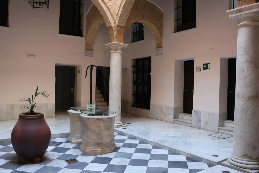Patio con columnas de mármol, solería blanca y negra, un brocal de pozo y una tinaja