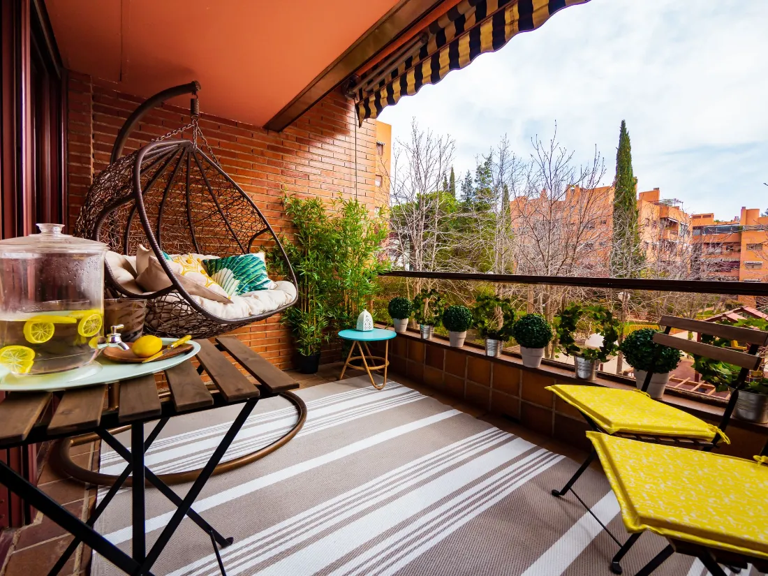 Terraza con toldo, sillón colgante, plantas y edificios de ladrillo enfrente