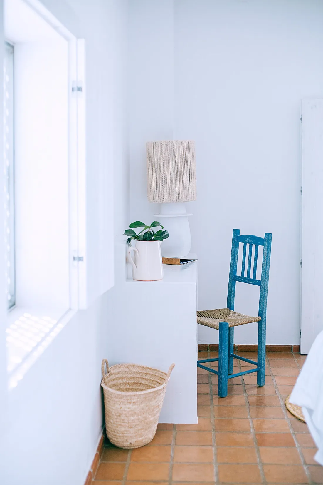 Habitación blanca con ventana al patio y una silla azul de enea