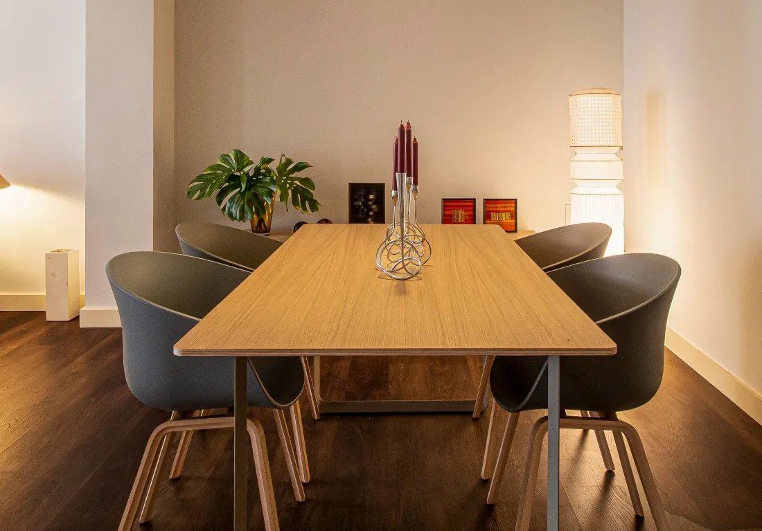 Comedor con mesa de madera clara, sillas grises y luz cálida