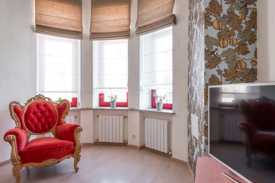 Mirador de tres ventanas con estores y un sillón rojo tapizado delante